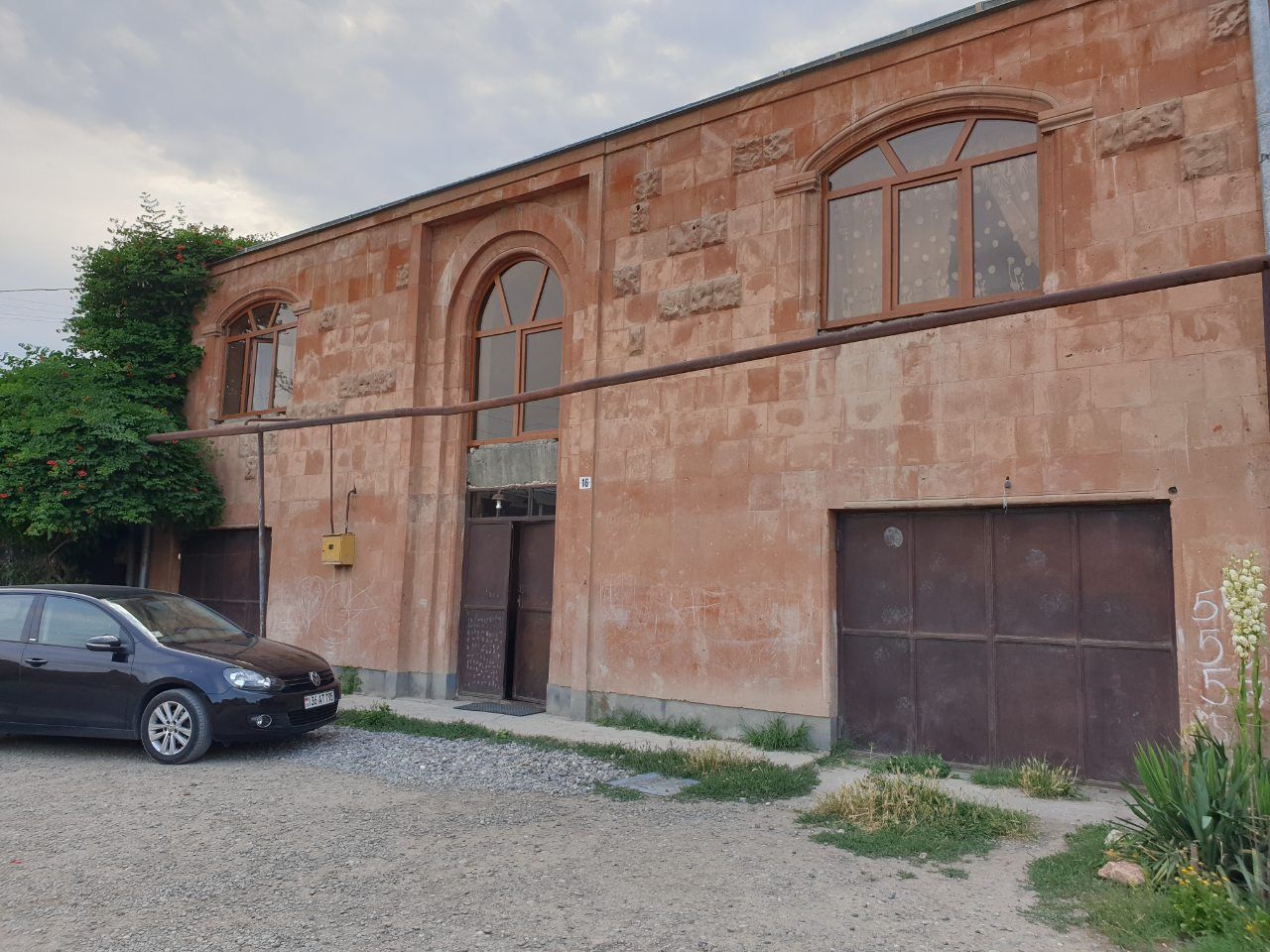 Bâtiment en briques de deux étages avec des fenêtres cintrées, des portes marron et une voiture garée.