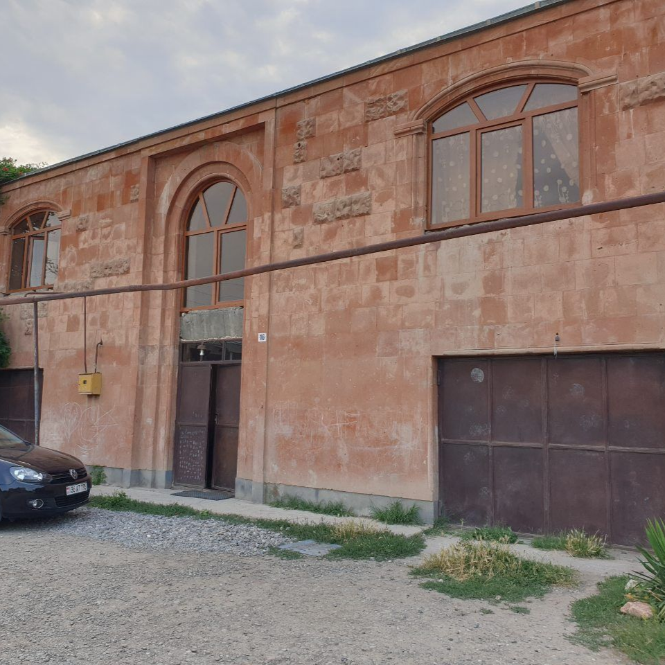 Extérieur d'un bâtiment couleur pêche avec des fenêtres cintrées, une porte en métal et une voiture garée.