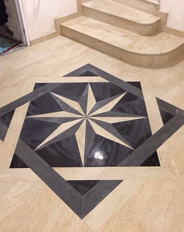 Incrustation complexe de carreaux noirs et blancs en forme d'étoile sur un sol beige, avec un escalier en pierre en arrière-plan.