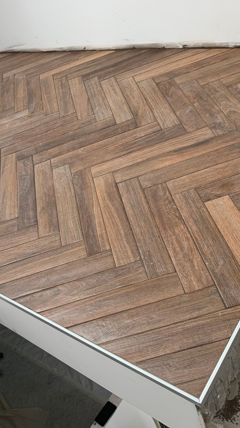 Carrelage imitation bois à chevrons avec bordure métallique.