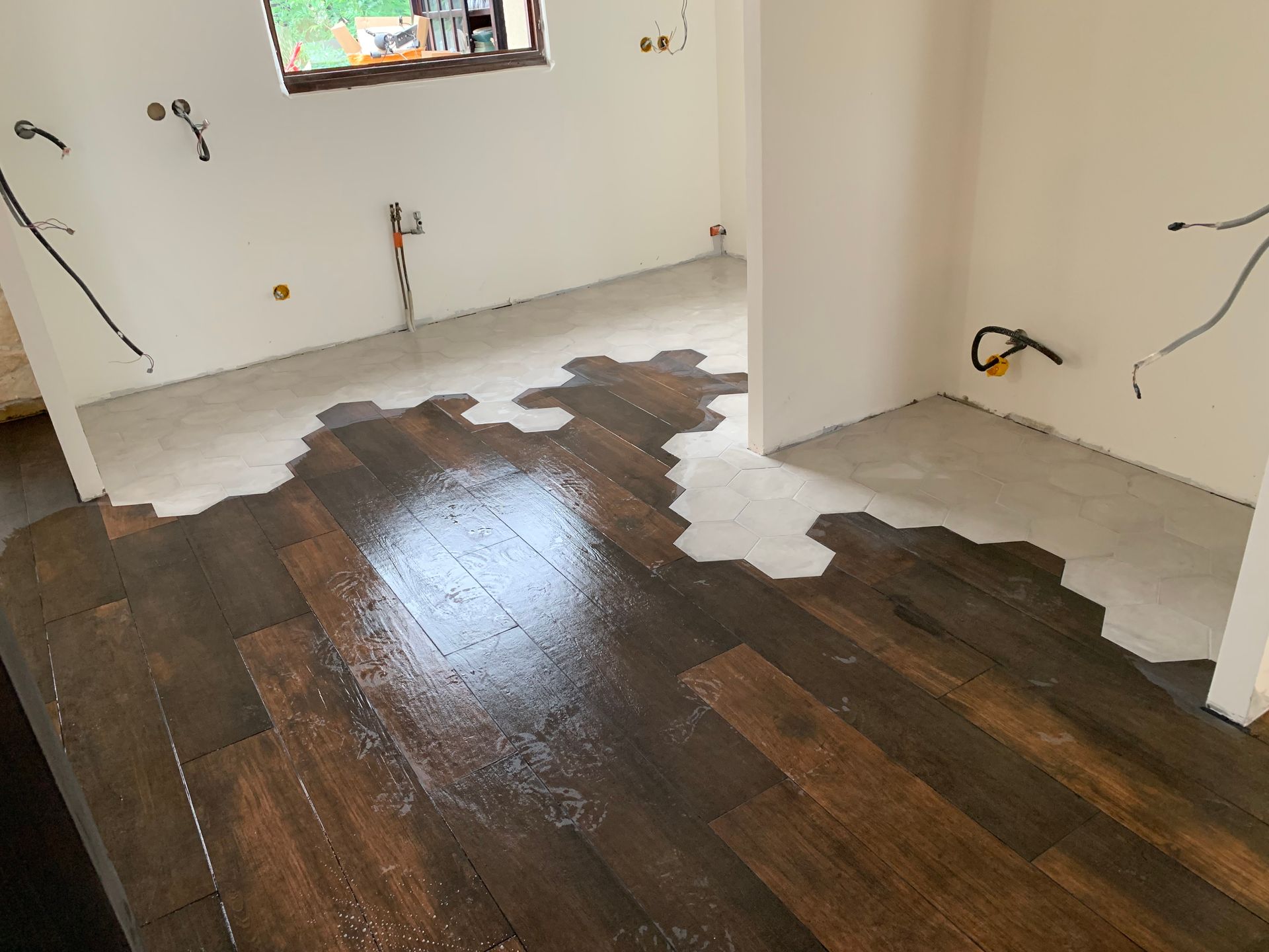 Plancher en bois partiellement installé, tache foncée sur le bois, sous-plancher en béton visible, travaux en cours.