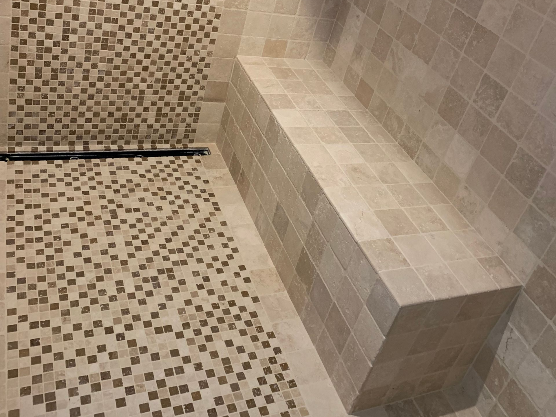Douche carrelée avec banquette intégrée. Les murs, le sol et la banquette sont recouverts de carreaux beiges et marron.