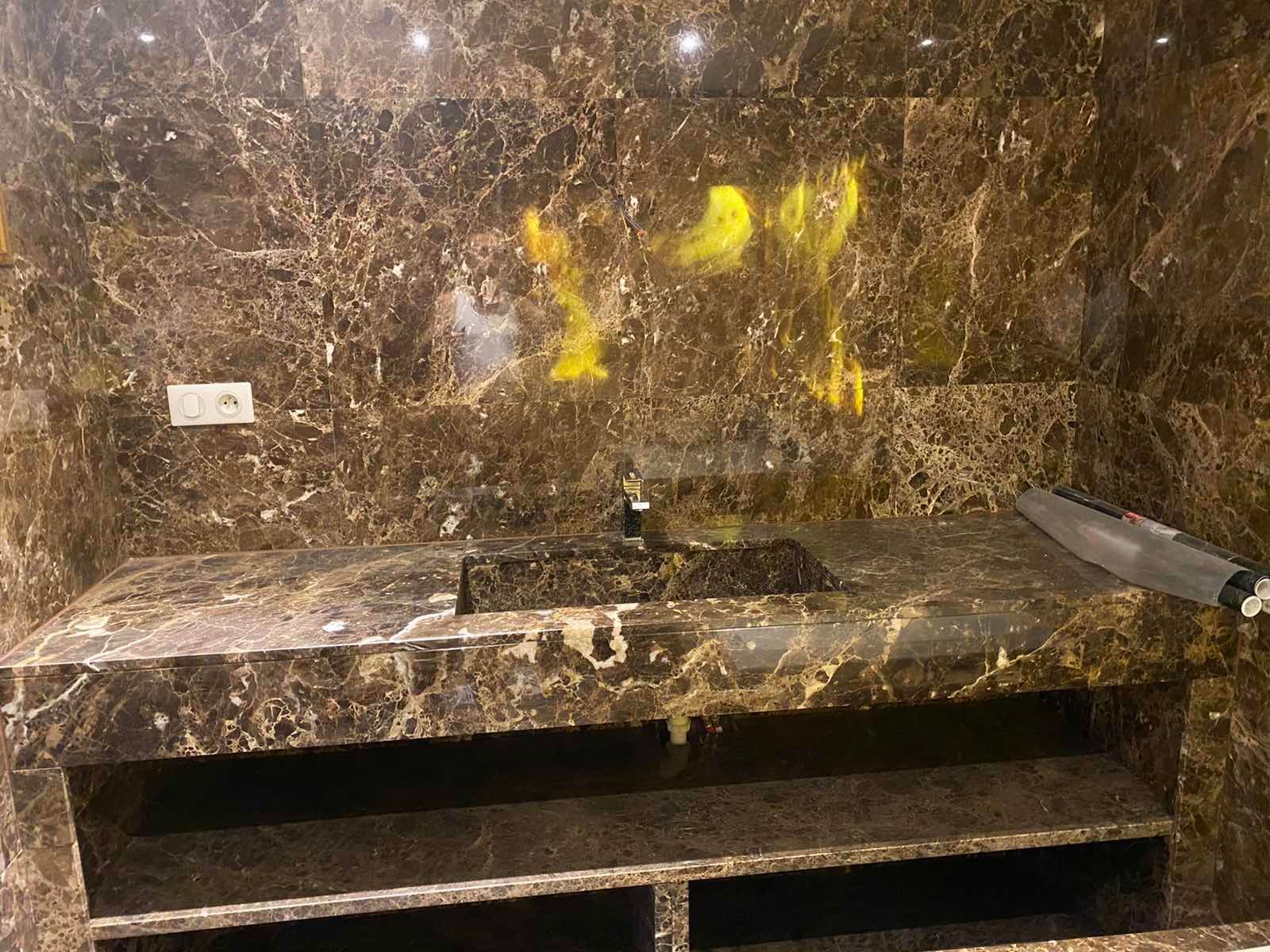 Salle de bains en marbre brun avec lavabo, graffitis à la peinture en aérosol sur le mur.