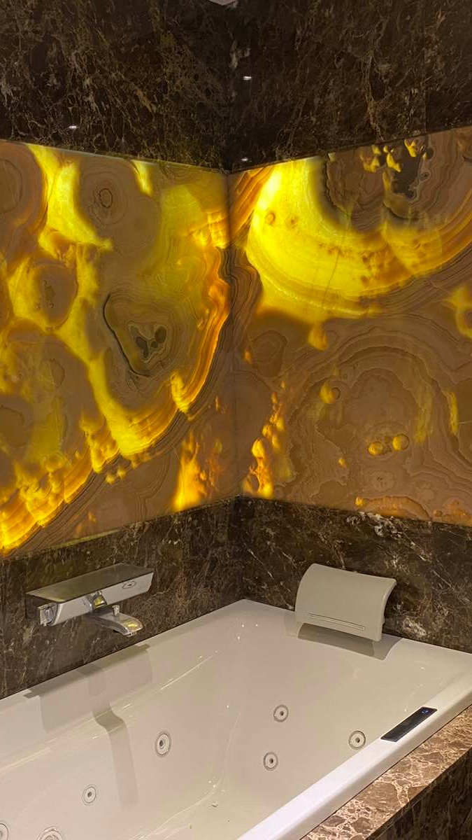 Baignoire d'angle avec murs en onyx brun doré rétroéclairés et garnitures en marbre brun foncé.