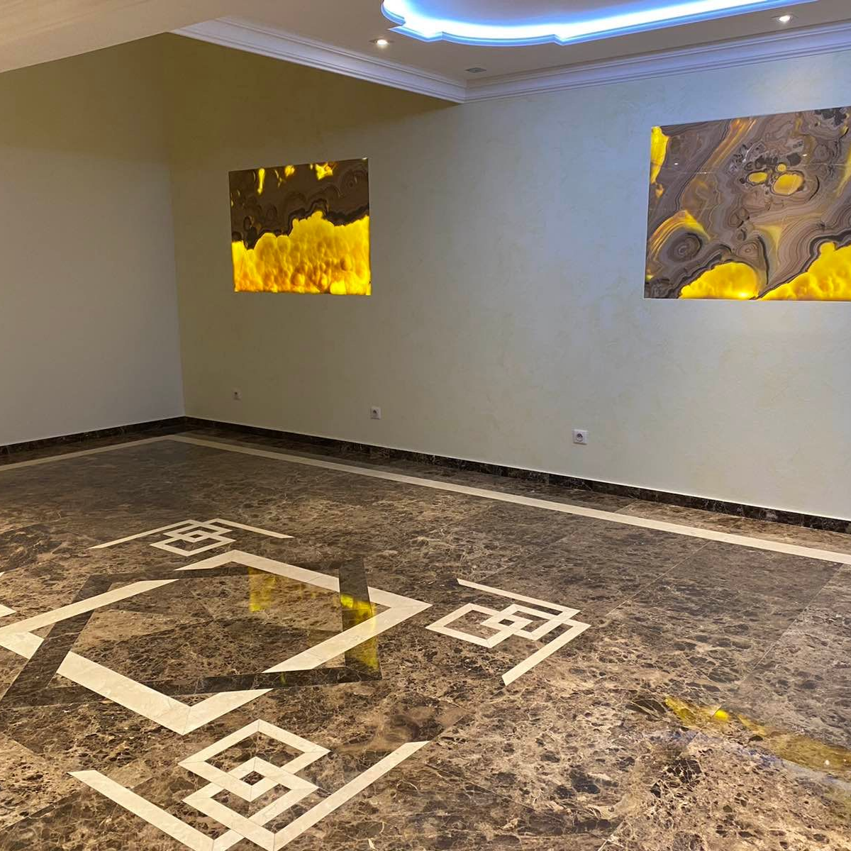 Pièce avec sol en marbre, incrustations décoratives et deux œuvres d'art abstraites éclairées par-derrière.