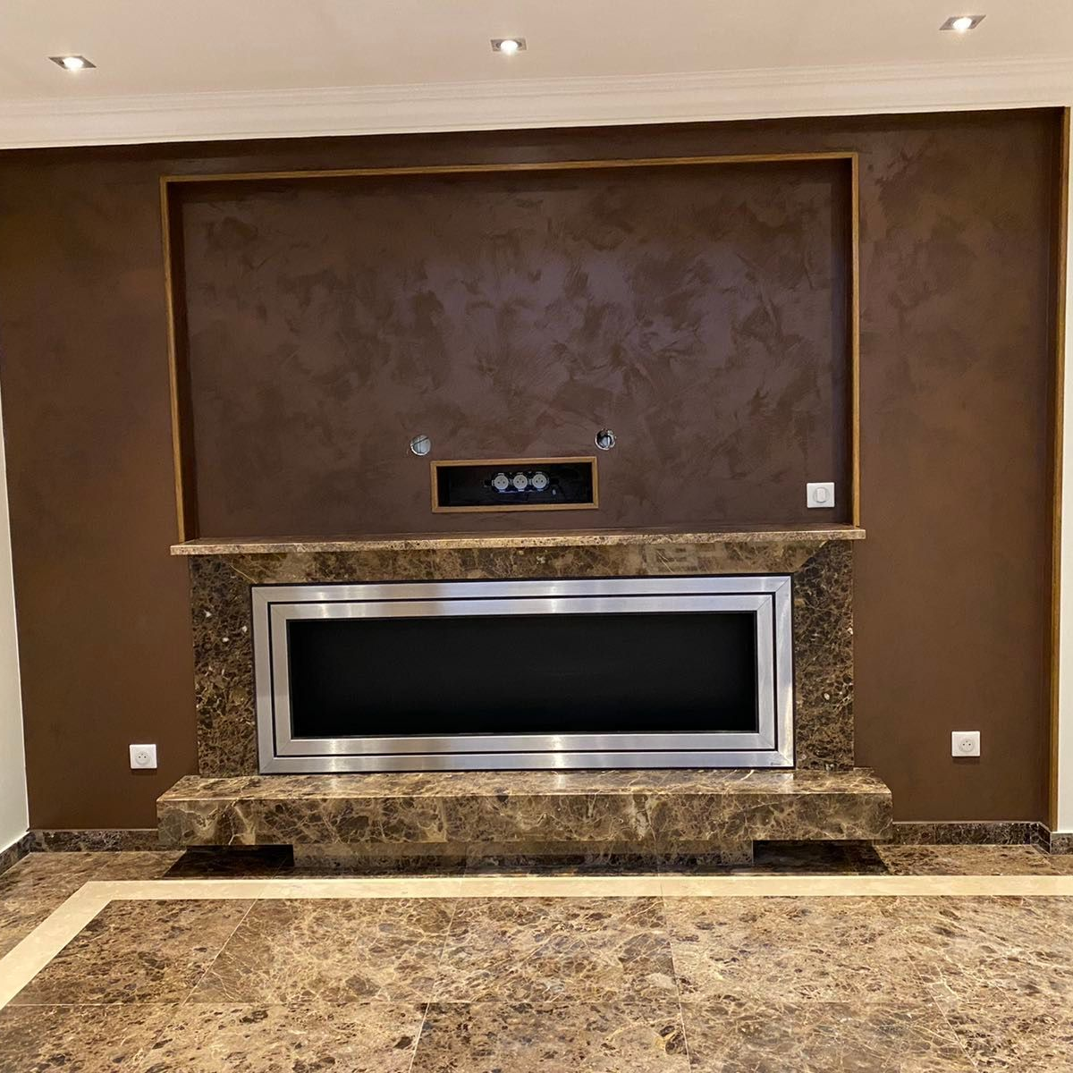 Mur brun avec cheminée intégrée. Foyer et mur d'enceinte en marbre brun, centre sombre avec cheminée en acier inoxydable.