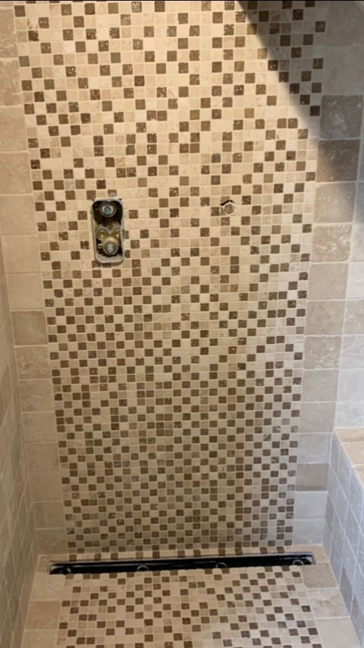 Douche avec frise décorative en mosaïque, commandes et caniveau linéaire.