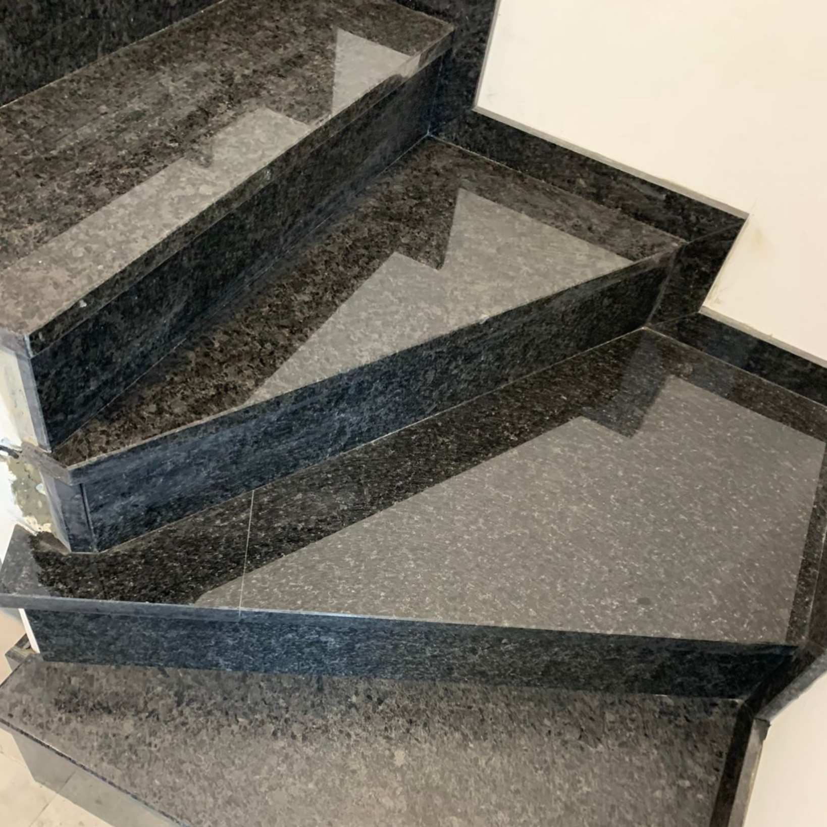 Escalier en granit avec marches gris foncé et murs blancs.