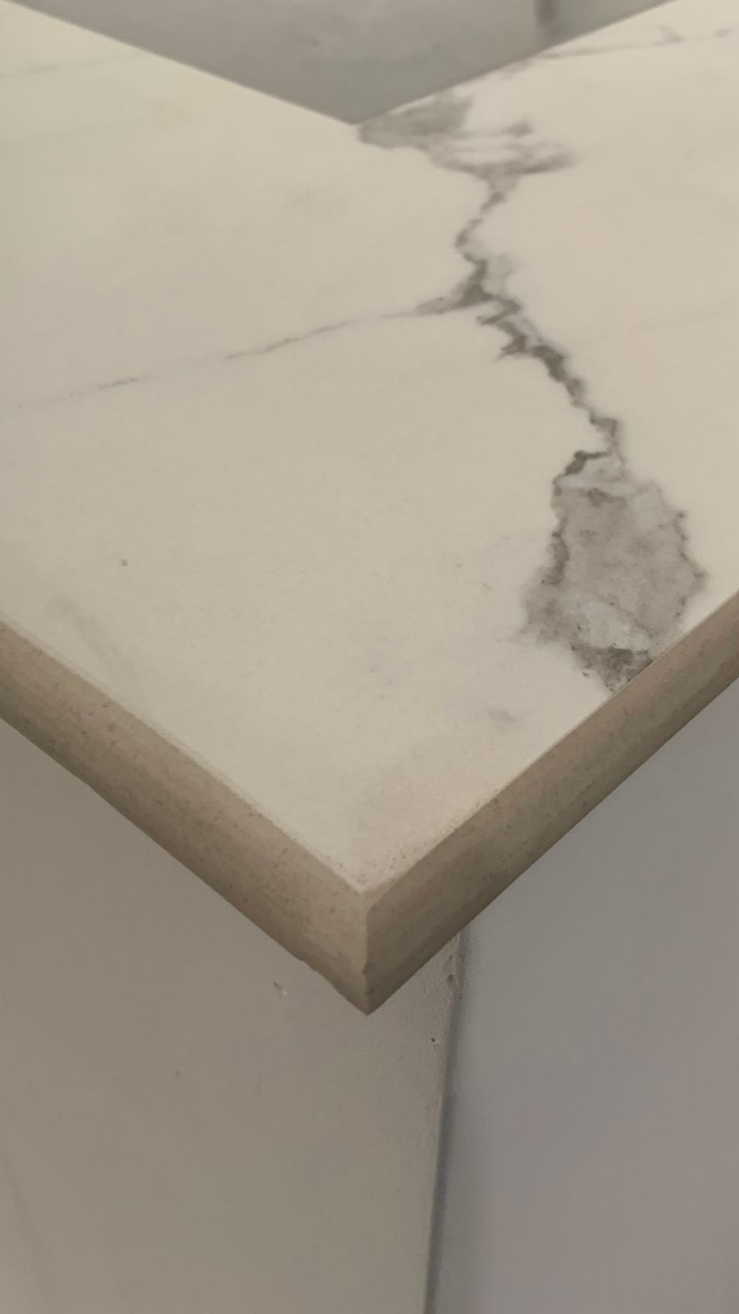 Gros plan sur le bord d'un comptoir en marbre blanc veiné de gris et présentant un bord lisse et biseauté.