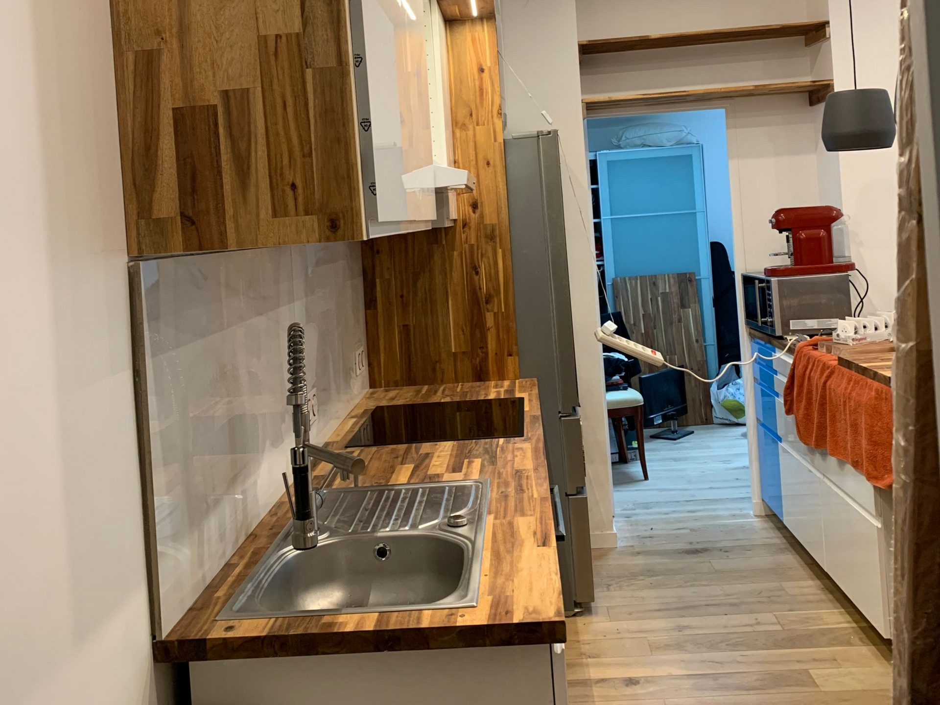 Petite cuisine avec comptoirs et armoires en bois, évier en acier inoxydable et réfrigérateur.