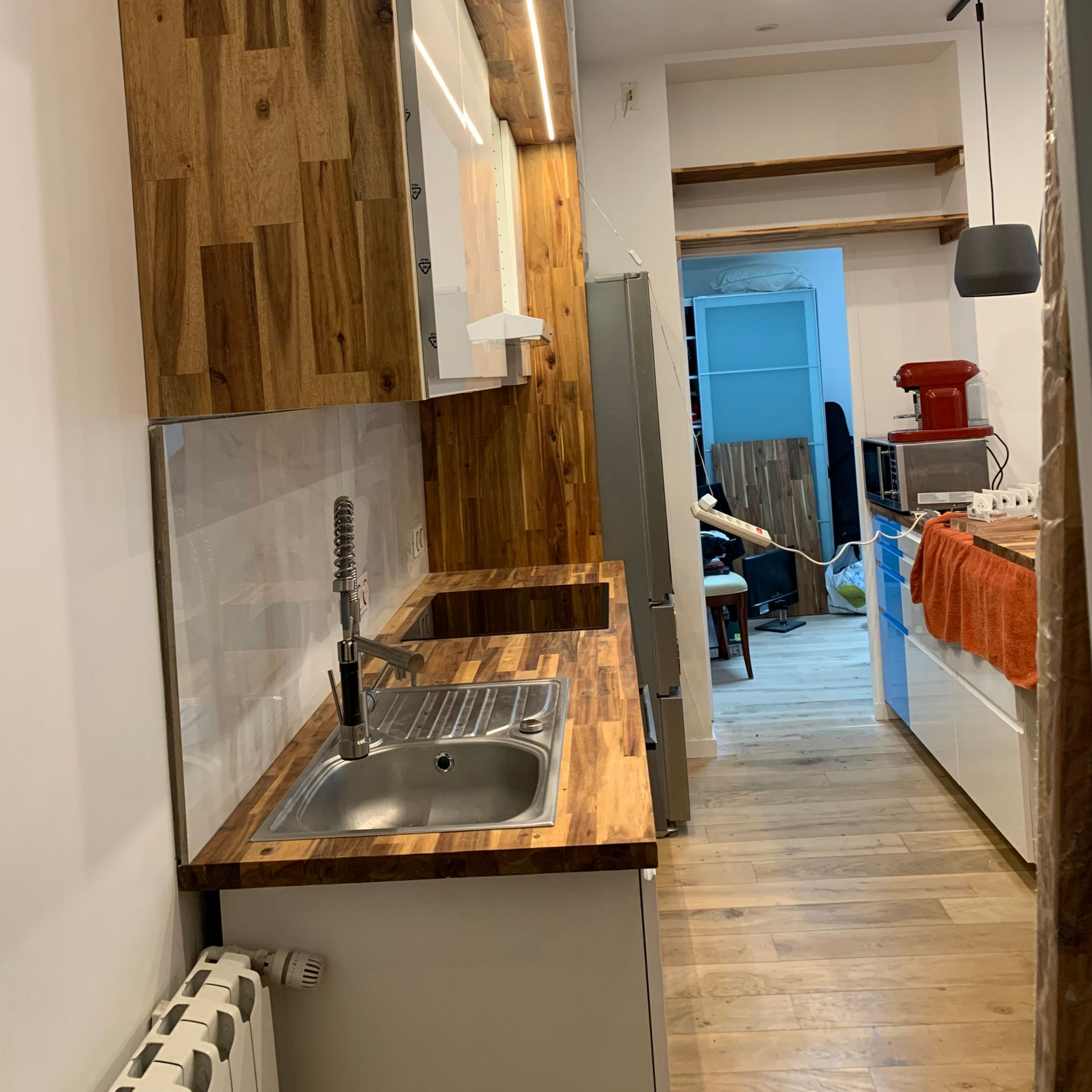 Une cuisine étroite avec des placards clairs, des plans de travail en bois, un évier en inox et un réfrigérateur.