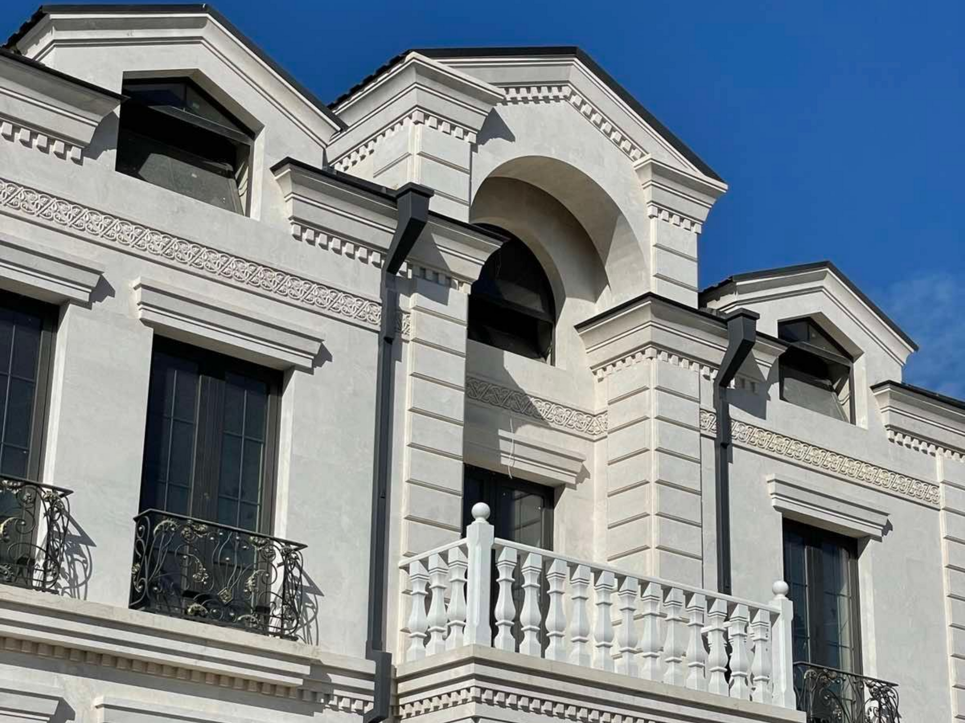 Bâtiment blanc aux ornements travaillés et aux fenêtres sombres se détachant sur un ciel bleu.