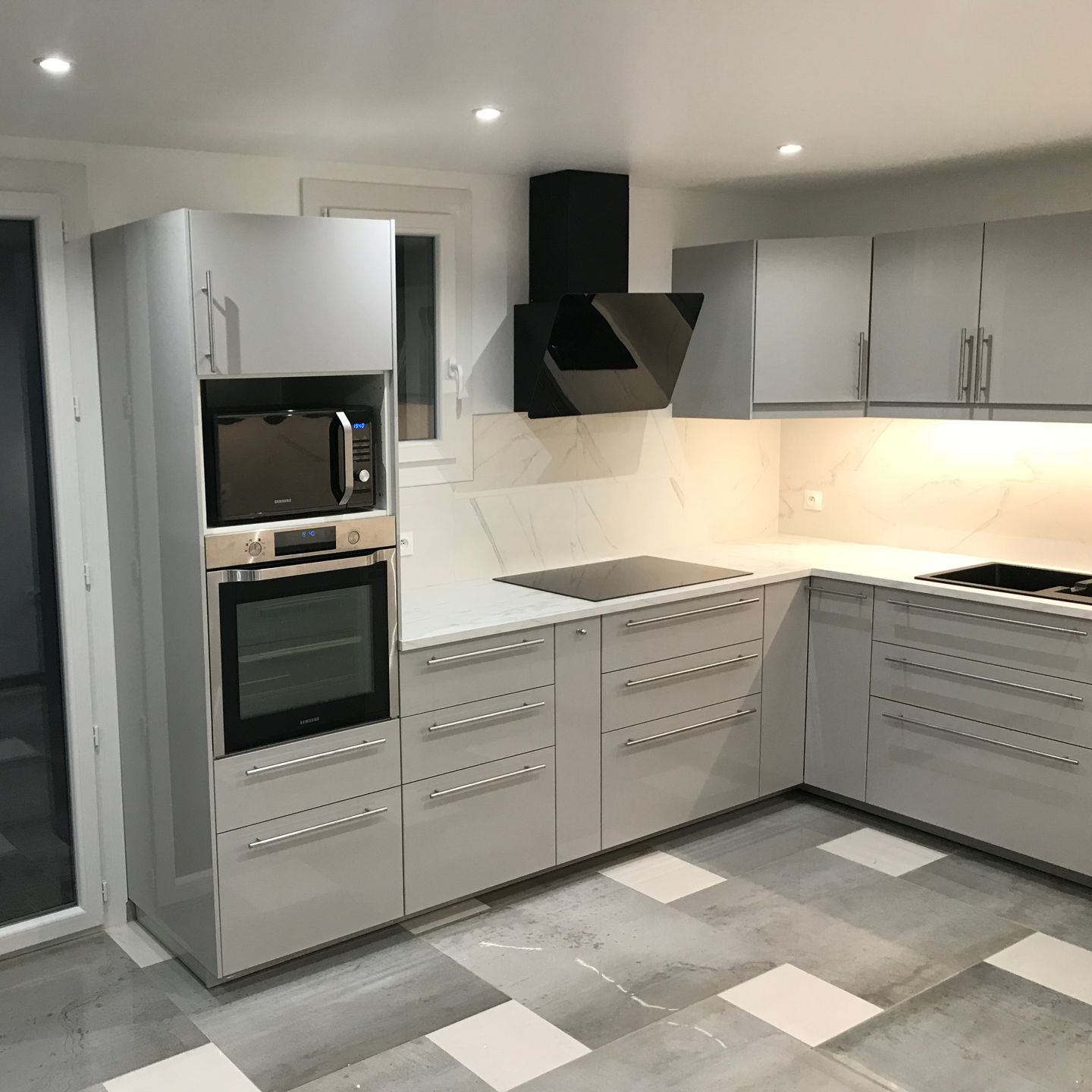 Cuisine moderne grise avec four encastré, micro-ondes et hotte aspirante, et un plan de travail en marbre.