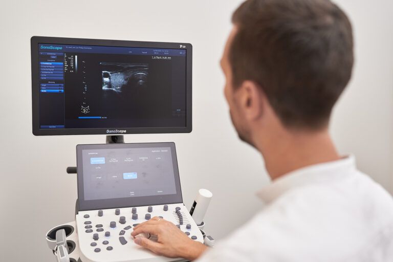 Mann bedient ein Ultraschallgerät und sieht sich in einer Arztpraxis einen medizinischen Scan auf dem Bildschirm an.