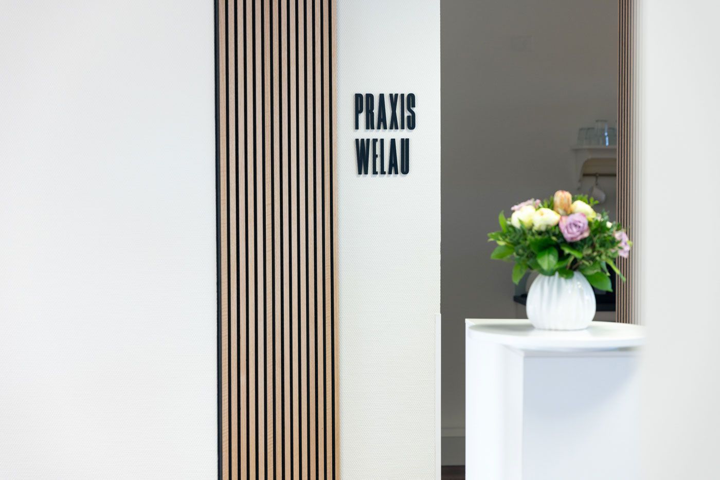 Fünf Personen in weißen Hemden und Jeans/Hosen sitzen auf einem grauen Sofa vor einer Wand mit einer Zeichnung.