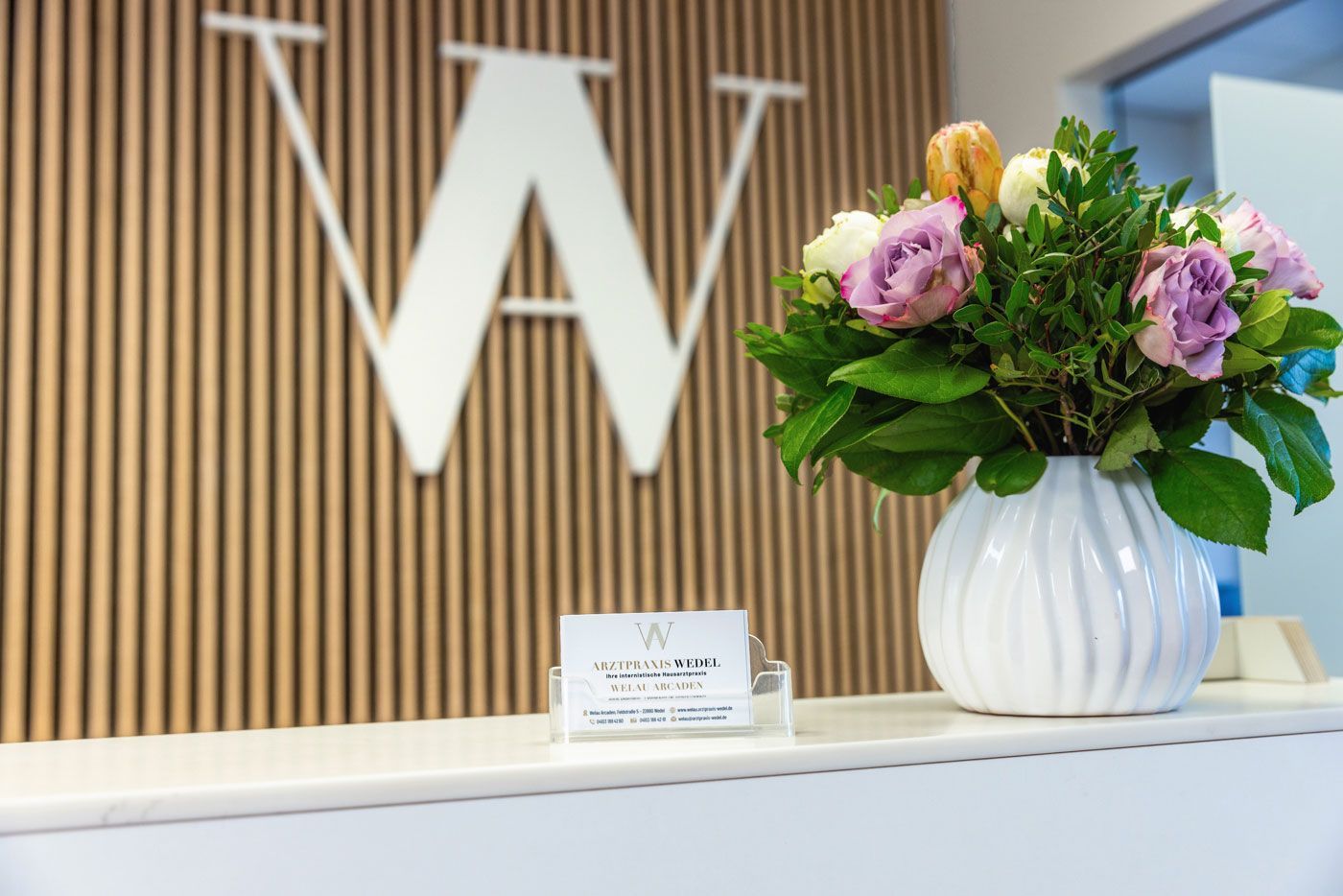 Empfangsbereich mit weißem Empfangstresen, Holzlamellenwand mit 