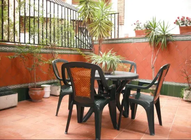 Pequeño patio con mesa y sillas de plástico verde, plantas en macetas y pared de estuco rojo.