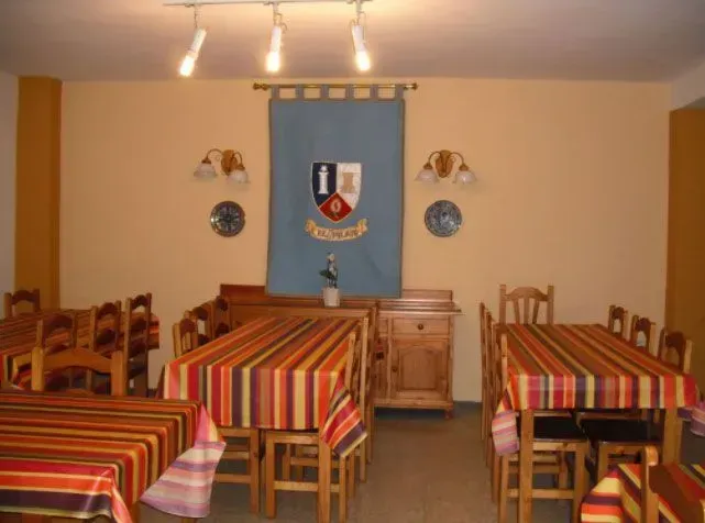 Comedor con mantelería de rayas, muebles de madera y pancarta con escudo en la pared.