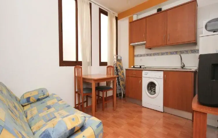 Apartamento pequeño con cocina, comedor y sofá. Armarios marrones, lavadora y una mesa pequeña.