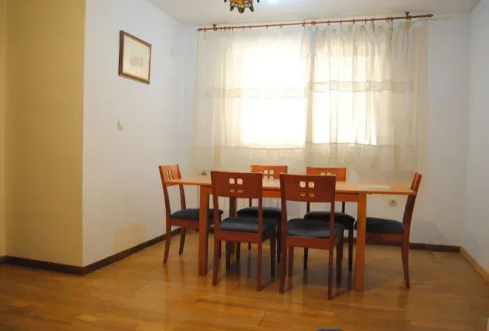 Comedor con mesa de madera y seis sillas cerca de una ventana con cortinas transparentes.