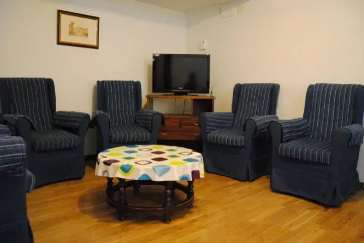 Un círculo de sillones azules rodea una mesa de café frente a un televisor y un mueble de madera en una habitación.