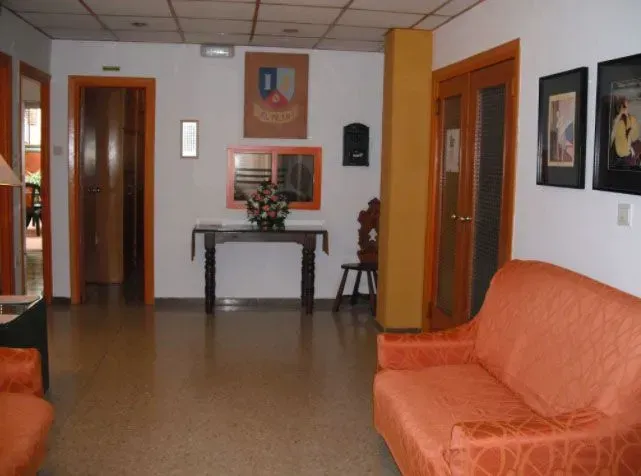 Lobby con sofá naranja, puertas de madera, mesa con flores y obras de arte enmarcadas.