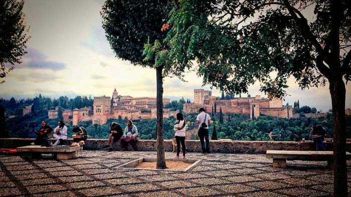La gente se sienta en los bancos, mirando la Alhambra en Granada, España, a través de los árboles.