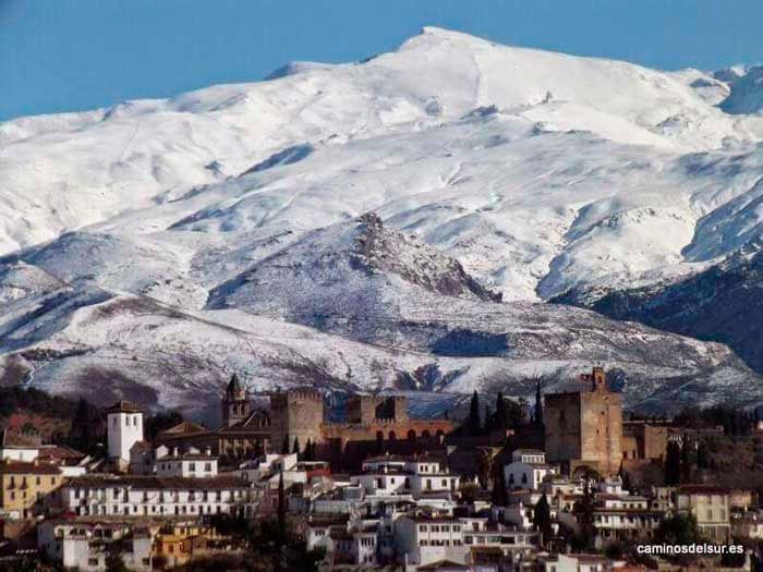 Montañas cubiertas de nieve se elevan sobre el palacio de la Alhambra y Granada, España, en un día soleado.