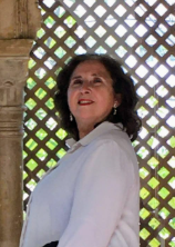 Mujer con top blanco, sonriendo, mirando hacia arriba, frente a una estructura enrejada con vegetación.