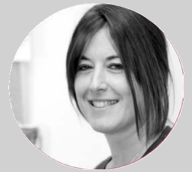 Mujer con cabello oscuro sonriendo, mirando al espectador; fondo borroso.