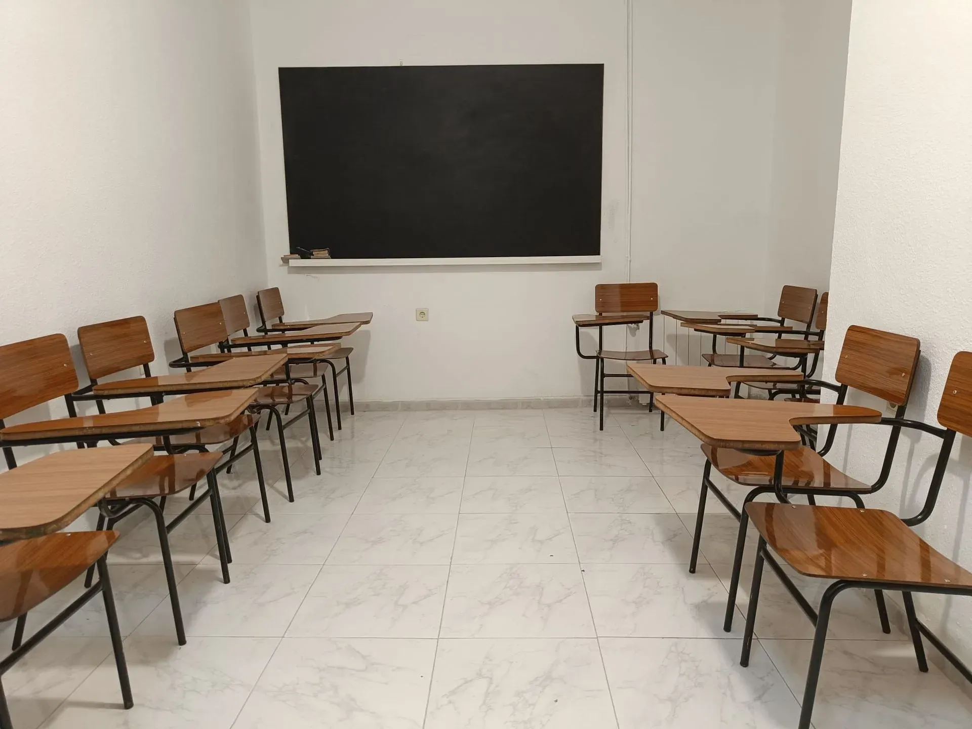 Aula con pupitres dispuestos en filas, pizarra en la pared.