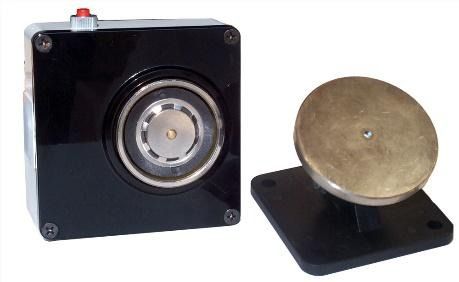 Una caja negra con un botón rojo encima y un objeto de latón al lado.