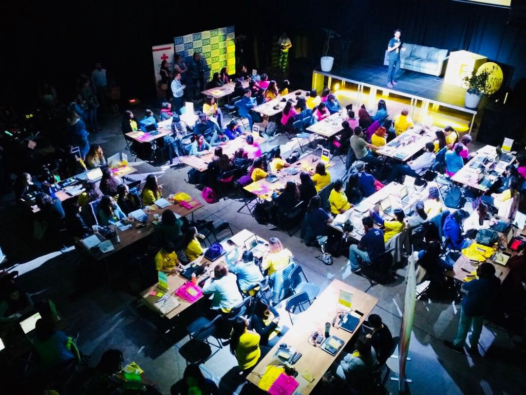 Un grupo grande de personas están sentadas en mesas en una habitación oscura.