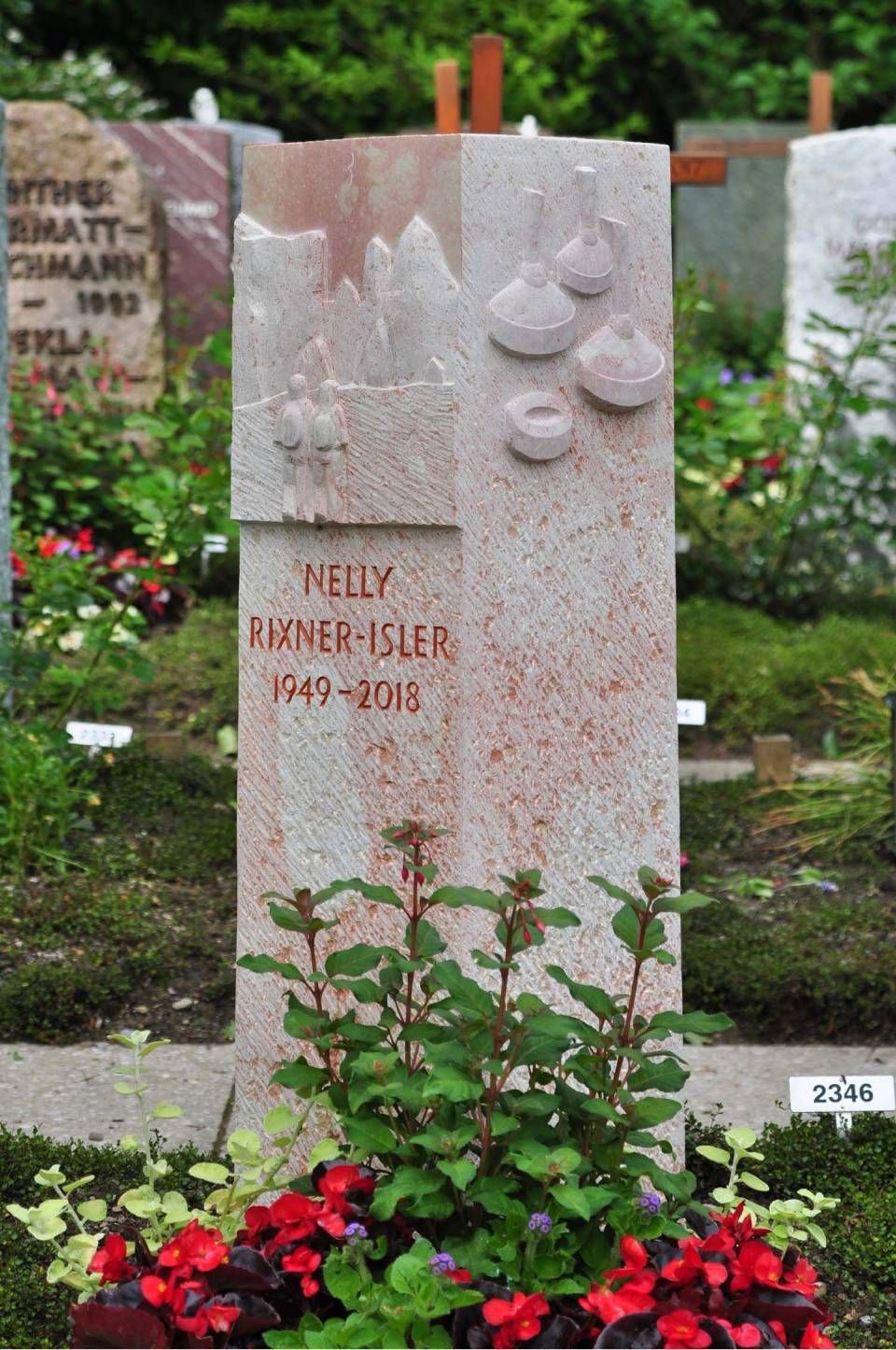 Gedenkgrabstein mit Blumen am Sockel auf einem Friedhof, eingraviert mit „Nelly“ und einem Vogelmotiv