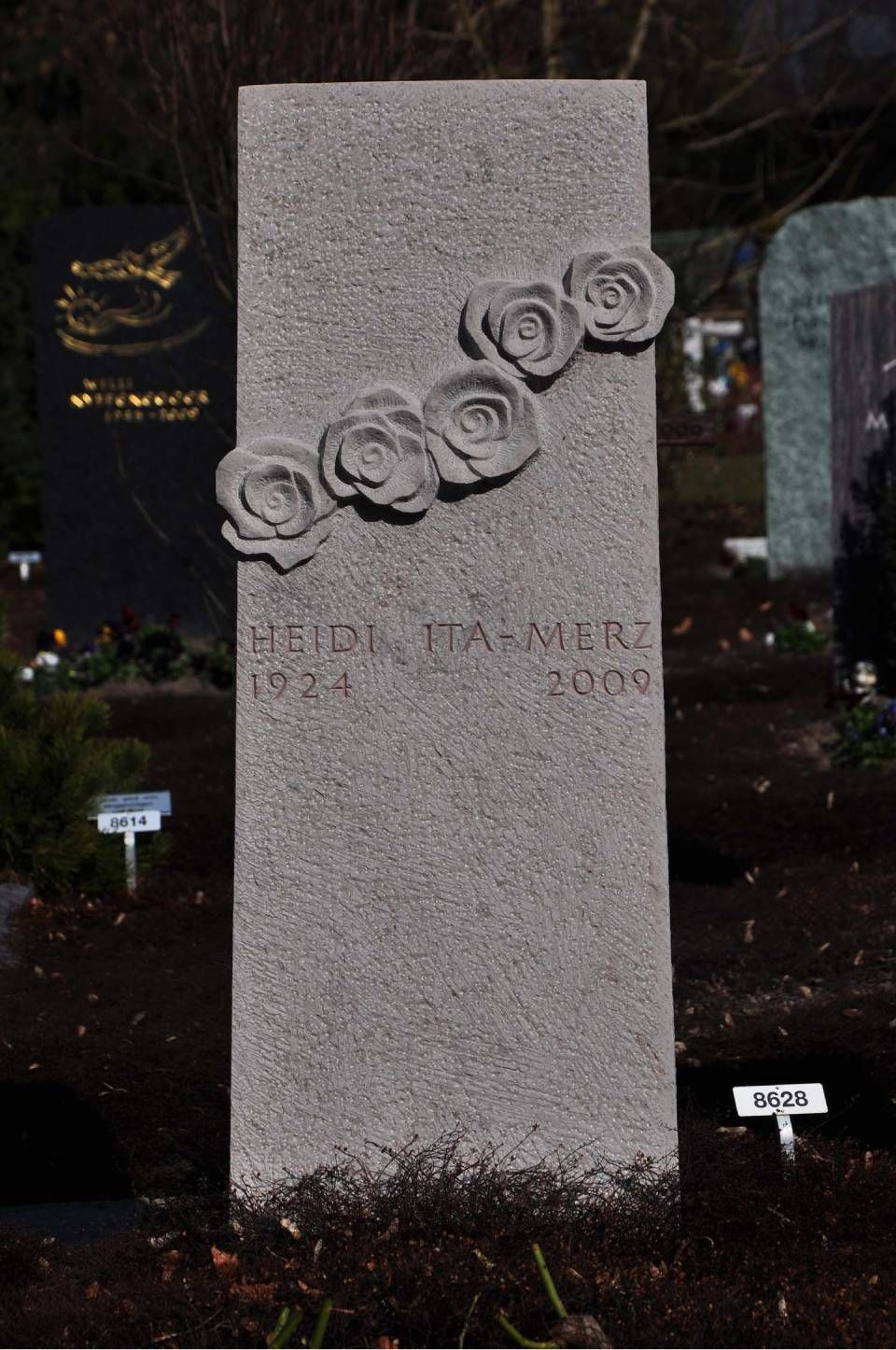 Grauer, aufrechter Grabstein mit eingravierten Rosen auf einem Friedhof bei Nacht
