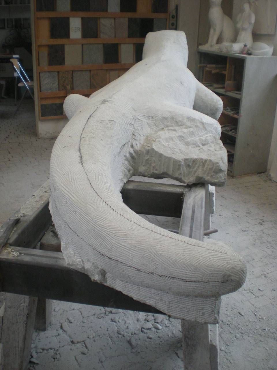 Weisse Gipsfigur in Form einer zusammengerollten Schlange auf einem Werkstatttisch, im Hintergrund Regale.