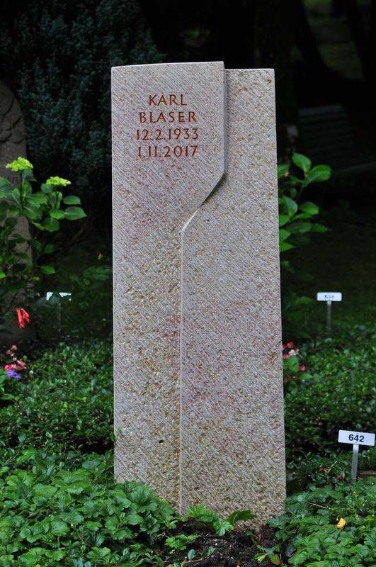 Hoher, rosafarbener Granitgrabstein in einem Garten, eingraviert mit dem Namen Karl Lagerfeld.