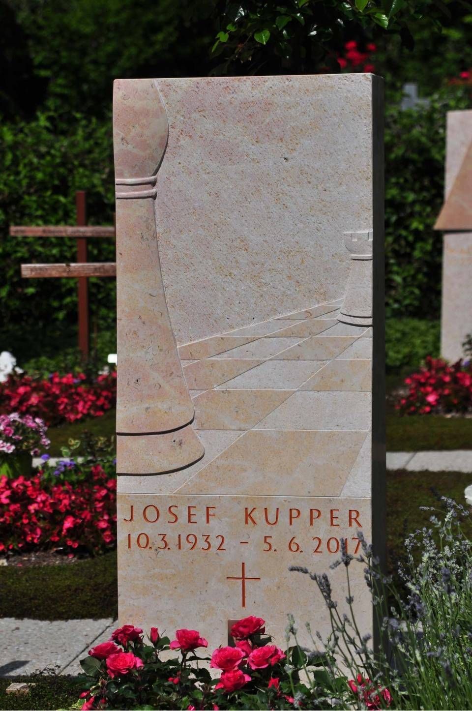 Steingrabstein auf einem Friedhof mit eingraviertem Namen und Daten, umgeben von Blumen und Grün