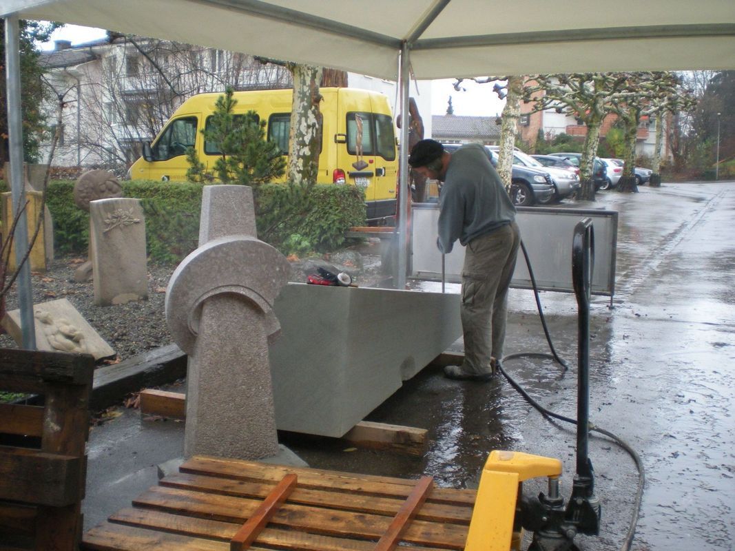 Behandschuhte Hände benutzen eine türkisfarbene Kettensäge, um eine weisse Wand zu durchtrennen, wobei Staub aufgewirbelt wird.