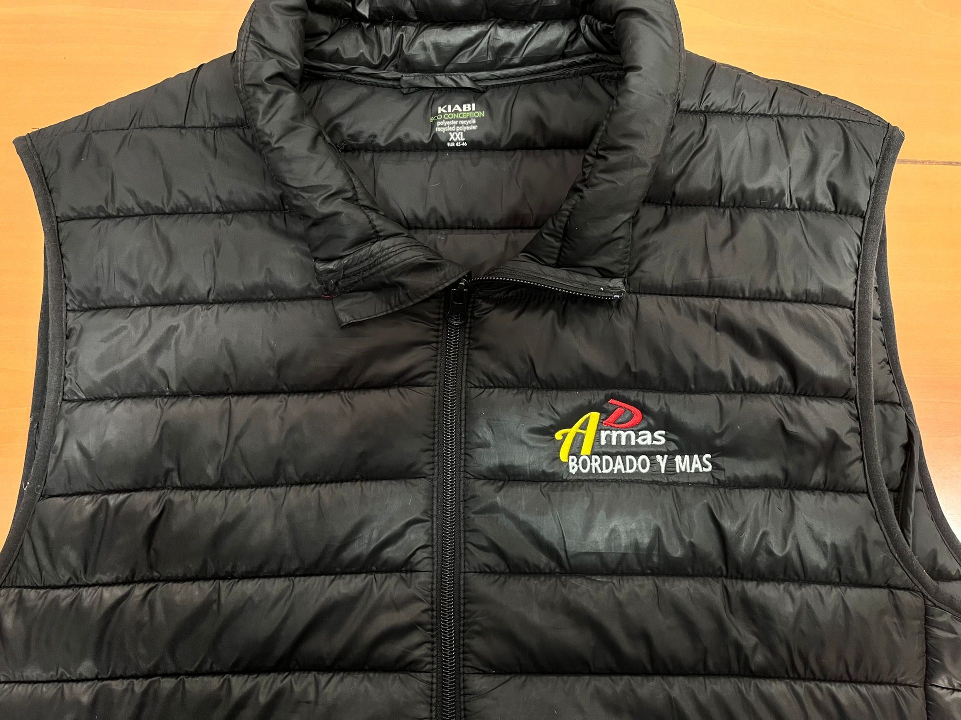 Un chaleco negro con un logo está sobre una mesa de madera.