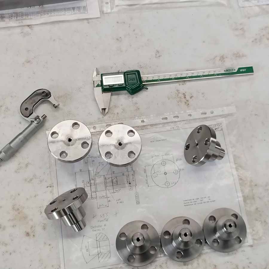 Un calibrador digital está sobre una mesa junto a un montón de piezas de metal.