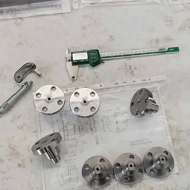 Un calibrador digital está sobre una mesa junto a un montón de piezas de metal.