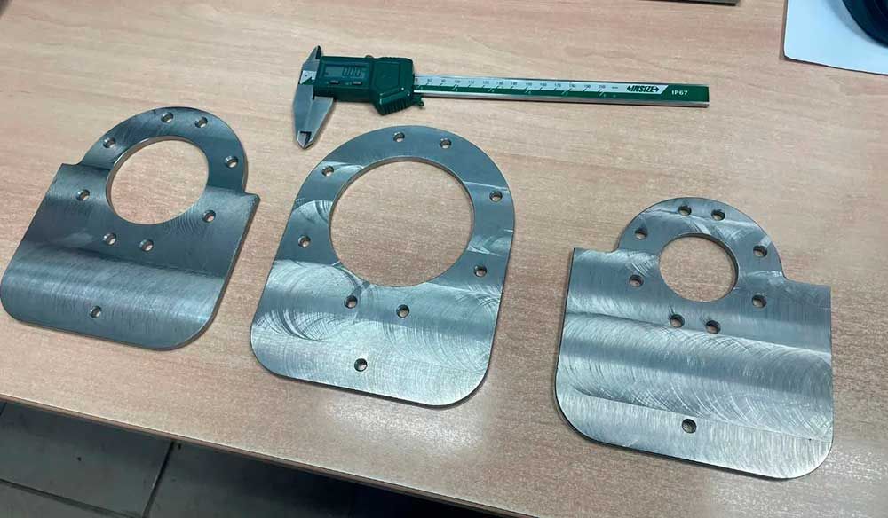 Tres piezas de metal están sobre una mesa de madera al lado de un calibrador.