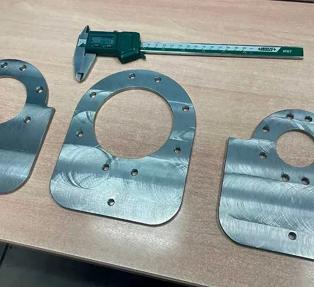 Un calibrador está colocado encima de una mesa de madera al lado de tres placas de metal.