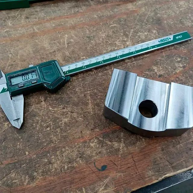 Un calibrador digital está sobre una mesa de madera al lado de un trozo de metal.