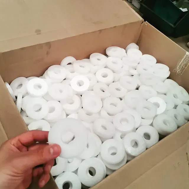 Una persona sostiene una caja llena de anillos de plástico blanco.
