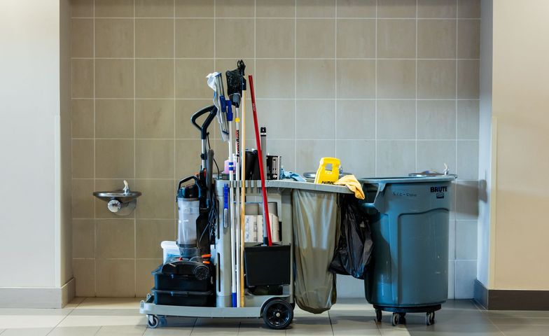 Chariot de nettoyage professionnel avec outils et poubelles à côté d'un lavabo mural dans une pièce carrelée