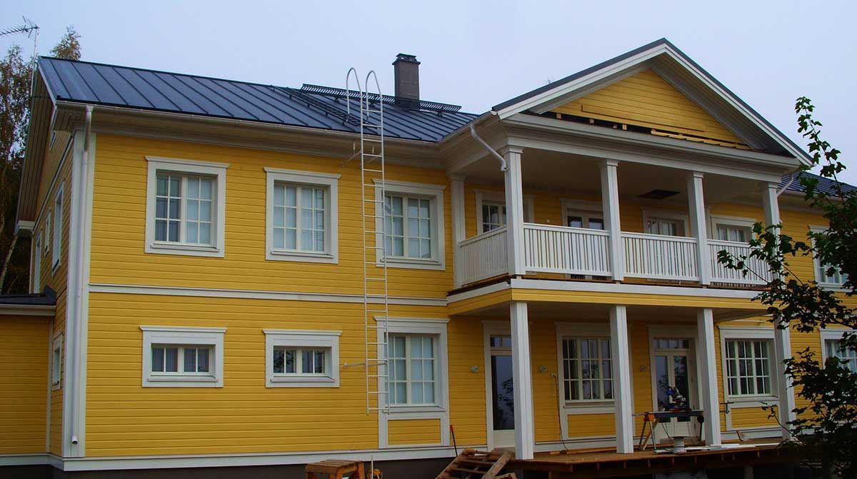 Keltainen kaksikerroksinen talo, jossa on valkoinen verhoilu ja parvekkeet tumman katon alla