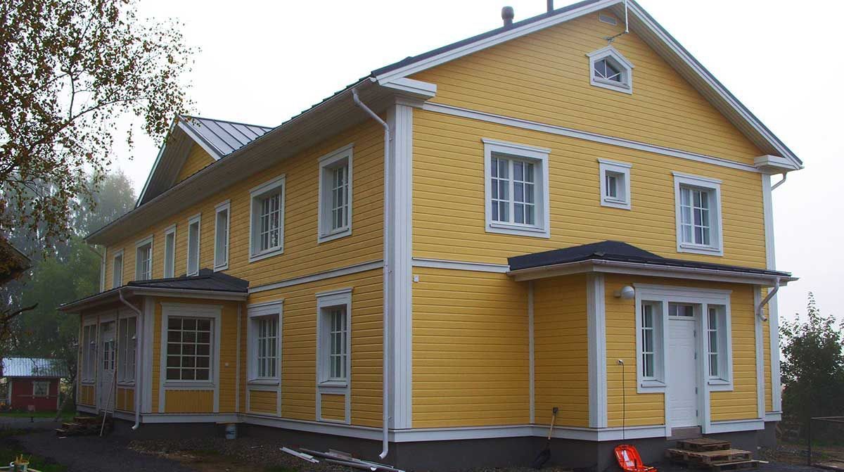Keltainen puutalo valkoisilla reunuksilla ja katetulla kuistilla sateisena päivänä
