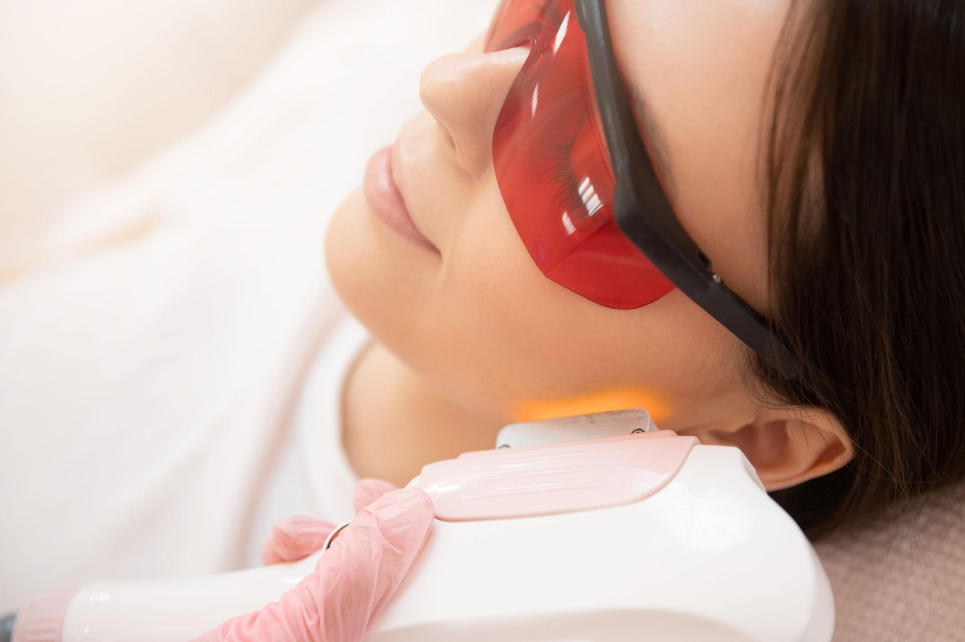 Persona recibiendo fototerapia en el cuello con un dispositivo portátil y una cubierta protectora roja para los ojos.